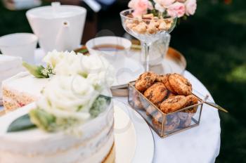 Table setting, tea party, closeup view on fresh sweets. Luxury silverware on white tablecloth, tableware outdoors. Wedding celebration on summer meadow
