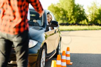 Male instructor and woman in car, traffic cones, lesson in driving school. Man teaching lady to drive vehicle. Driver's license education