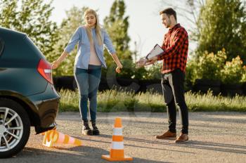Male instructor and woman at the car and downed cone, lesson in driving school. Man teaching lady to drive vehicle. Driver's license education