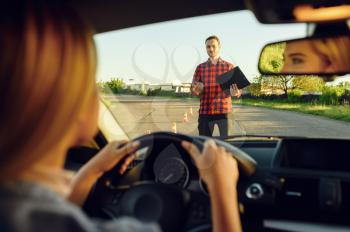 Woman in the car, instructor with checklist on road, driving school. Man teaching lady to drive vehicle. Driver's license education