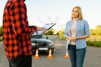 Woman and instructor with checklist on road, lesson in driving school. Man teaching lady to drive vehicle. Driver's license education