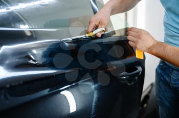 Male wrapper holds sunscreen film, car tinting service. Worker applying vinyl tint on vehicle window in garage