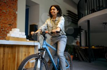 Pretty female student poses on bicycle in cafe. Woman learning a subject in coffeehouse, education and food. Girl studying in campus cafeteria