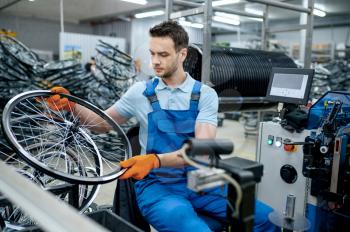 Mechanic in uniform works with bicycle wheel on factory. Bike rims and spokes assembly in workshop, cycle parts installation