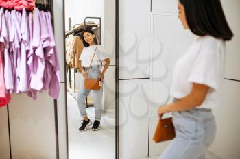 Cheerful woman choosing handbag in clothing store. Female person shopping in fashion boutique, shopaholic, shopper looking in mirror
