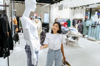 Cheerful woman standing at the mannequin, clothing store. Female person shopping in fashion boutique, shopaholic, shopper looking on garment
