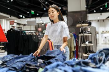 Cheerful woman choosing jeans in clothing store. Female person shopping in fashion boutique, shopaholic, shopper looking on garment