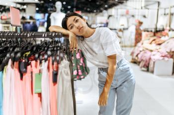 Tired woman at the rack in clothing store. Female person shopping in fashion boutique, shopaholic, shopper looking on garment