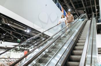 Two girls on escalator, clothing store. Women shopping in fashion boutique, shopaholics, shoppers in clothes center