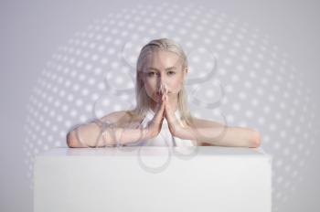 Futuristic young woman in white clothes at cube, light grey background. Female person in virtual reality style, future technology, futurism concept