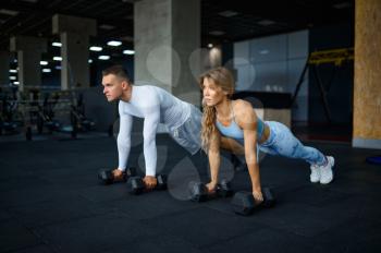 Sportive couple doing push-ups with dumbbells, training in gym. Athletic man and woman on workout in sport club, active healthy lifestyle