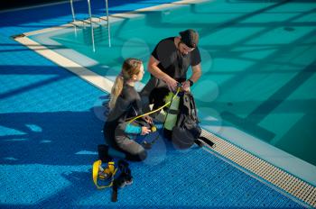 Male instructor in suit explains how scuba gear works, diving school. Teaching people to swim underwater, indoor swimming pool interior