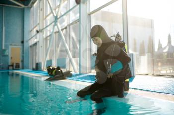 Male diver in scuba suit sitting at the poolside, diving school. Teaching people to swim underwater, indoor swimming pool interior on background