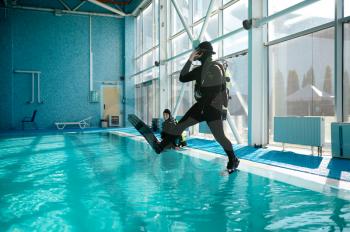 Diver in scuba gear jumps into the pool, lesson in diving school. Teaching people to swim underwater, indoor swimming. Men with aqualangs