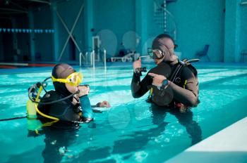 Female diver and male divemaster in scuba gear, lesson in diving school. Teaching people to swim underwater, indoor swimming pool interior on background