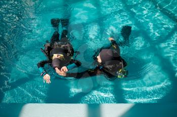 Female diver and male instructor in scuba gear, lesson in diving school. Teaching people to swim underwater, indoor swimming pool interior on background