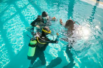 Divemaster and two divers in aqualungs, course in diving school. Teaching people to swim underwater with scuba gear, indoor swimming pool interior on background, group training