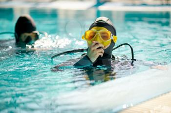 Female diver and male divemaster in scuba gear, dive lesson in diving school. Teaching people to swim underwater, indoor swimming pool interior on background
