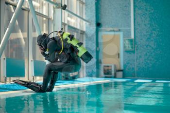 Male diver in scuba gear jumps into the pool, course in diving school. Teaching people to swim underwater, indoor swimming. Men with aqualangs