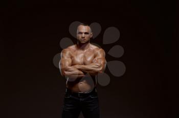 Male muscular athlete shows his power in studio, dark background. One man with athletic build, shirtless sportsman in jeans pants, active healthy lifestyle