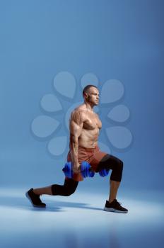 Male athlete with dumbbells, training in studio, blue background. One man with athletic build, shirtless sportsman in sportswear, active healthy lifestyle