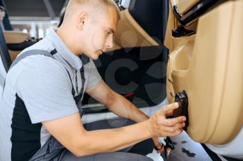 Worker with brush wipes car door trim, dry cleaning and detailing. Vehicle washing in garage, thoroughly care of automobile, chemical and vacuum clean service