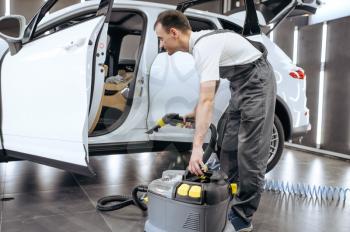 Worker removes dirt with vacuum cleaner, car dry cleaning and detailing. Vehicle washing service in garage, thoroughly care of automobile
