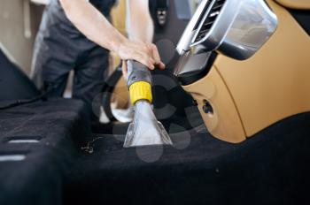 Worker cleans car interior with vacuum cleaner, car dry cleaning and detailing. Vehicle washing in garage, thoroughly care of automobile