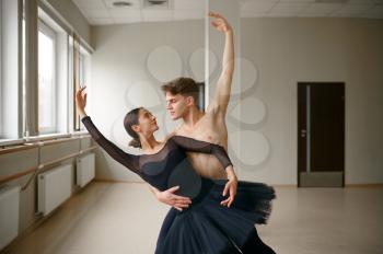 Female and male ballet dancers dancing at barre. Ballerina with partner training in class, dance studio interior on background