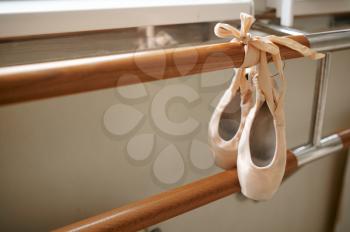 Pink ballet shoe with ribbon hanging on barre in dance class, nobody. Ballerina footwear, dance studio interior on background