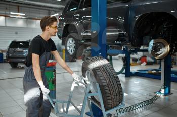 Male mechanic fixes problem with wheel, car service. Vehicle repairing garage, man in uniform, automobile station interior on background