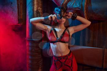 Sexy woman poses in bdsm suit and leather mask, abandoned factory interior on background. Young girl in erotic underwear, sex fetish, sexual fantasy