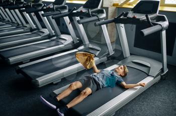 Tired youngster lying on treadmill in gym, running machine. Boy on training, health care and healthy lifestyle, schoolboy on workout