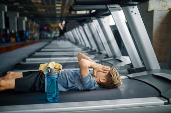 Tired youngster lying on treadmill in gym, running machine. Boy on training in sport club, health care and healthy lifestyle, schoolboy on workout