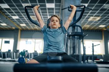Boy on exercise machine, front view, training in gym. Youngster in sport club, healthcare and healthy lifestyle, schoolboy on workout, sportive youth