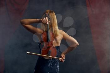 Female violonist with bow and violin behind her back, virtuoso performance on stage. Woman with string musical instrument, music art, musician play on viola, dark background