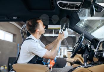 Worker watering car interior, dry cleaning and detailing. Vehicle washing in garage, thoroughly care of automobile, chemical and vacuum clean service