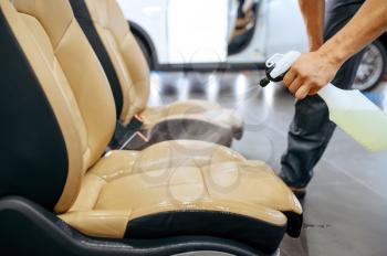 Worker with spray moisturizes car seats, dry cleaning and detailing. Vehicle washing in garage, thoroughly care of automobile, chemical and vacuum clean service