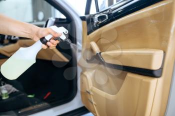 Worker sprays car door trim, dry cleaning and detailing. Vehicle washing in garage, thoroughly care of automobile, chemical and vacuum clean service