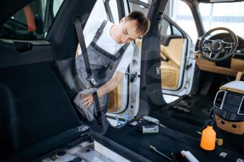 Worker with rag wipes car interior plastic, dry cleaning and detailing. Vehicle washing in garage, thoroughly care of automobile, chemical and vacuum clean service