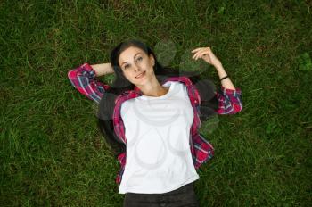 Young woman lying on grass in summer park, top view. Cheerful female person poses on lawn, picnic on the field in sunny day, girl on green meadow