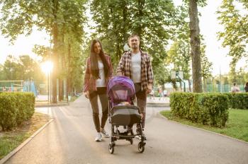 Young parents walks with little baby in summer park. Mom and dad leisures with male kid, picnic with child in the forest, family happiness