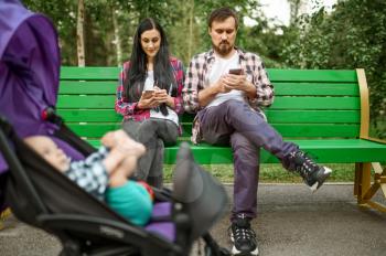 Parents using phones while walks with little baby in summer park. Mom and dad leisures with male kid, picnic with child in the forest, family happiness