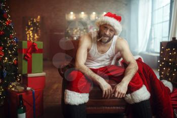 Vile Santa claus in red cap smoking cigar on couch, nasty party, humor. Unhealthy lifestyle, bearded man in holiday costume, new year and alcoholism