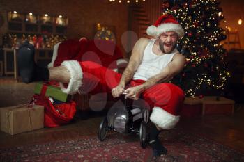 Bad drunk Santa claus in red hat riding on little toy car, nasty party, humor. Unhealthy lifestyle, bearded man in holiday costume, new year