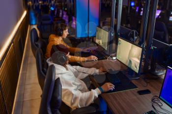 Two gamers in headsets play in gaming club. Virtual entertainment, e-sport tournament, cybersport lifestyle. Male person leisures in internet cafe