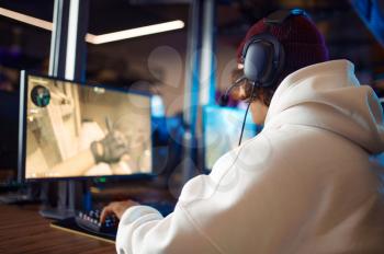 Young gamer in headset play shooter in game club. Virtual entertainment, e-sport tournament, cybersport lifestyle. Male person leisures in internet cafe