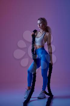 Young sportswoman with ropes poses in studio, neon background. Fitness woman at the photo shoot, sport concept, active lifestyle