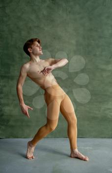 Male ballet dancer, training in dancing class, grunge wall on background. Performer with muscular body, grace and elegance of movements