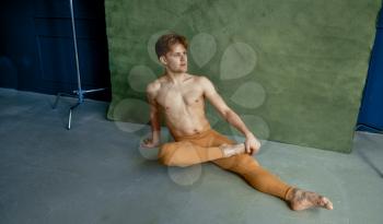 Male ballet dancer sittiing on the floor in dancing class, grunge wall on background. Performer with muscular body, grace and elegance of movements